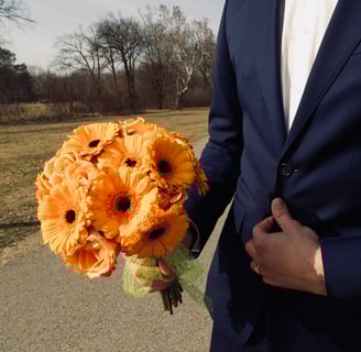Bărbat în costum bleumarin ținând un buchet cu gerbera portocalii.