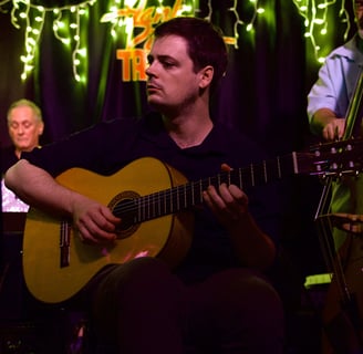 a man (rob coleman) playing acoustic guitar with a drummer and bassist