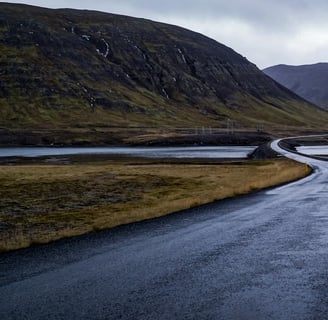 gray concrete road near green mountain under white clouds during daytime
