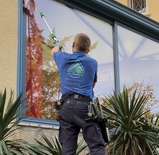 Un personne qui nettoie une vitre en hauteur à l'aide d'une perche