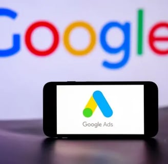 Celular en primer plano mostrando Google Ads, con una computadora desenfocada al fondo con "Google"