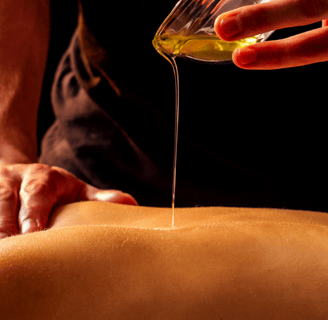 A hand pours oil from onto the back of a lying woman, another hand rests on the woman's shoulder