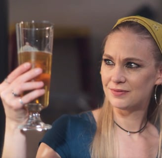 a woman in a blue shirt and a yellow headband holding a glass of beer