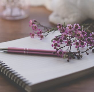pink pen on spiral notepad with pink flowers nearby