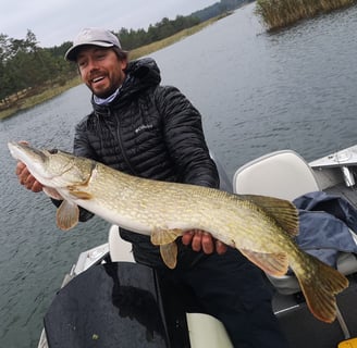 un homme est sur un bateau avec fishing escape sweden il à pêché un gros brochet en suède.