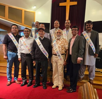 Nine South Asian fathers and father-figures wearing celebratory sashes, standing and smiling under a