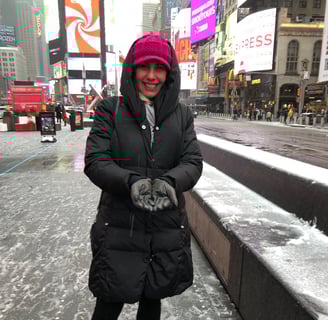 autora do blog, usando casaco comprido preto, e gorro pink em unma avenida com neve