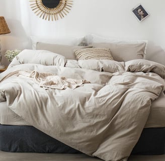 comfy bed with neutral tone bedding that looks lived in and a bit messy