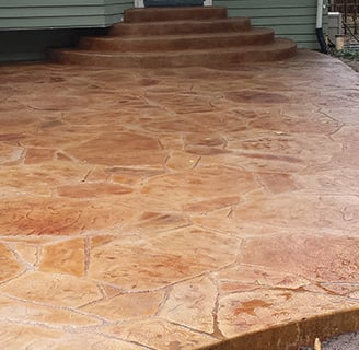 A beautiful brick colored stamped concrete patio with formed steps going up to the rear of a house