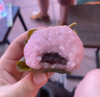 a person holding a pink sakura mochi with a anko inside