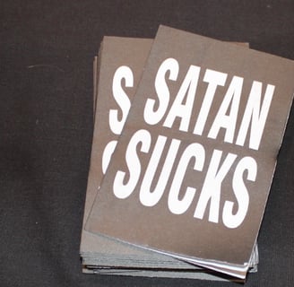 Free handouts at biker ministry table says “Satan Sucks.”