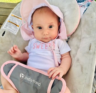 A newborn baby girl with a pink sunhat sitting in a bouncer, looking at the camera
