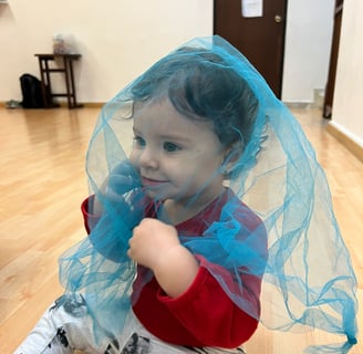 Niña sentada en piso de madera cubierta por una malla azul transparente en Ukelele Jardín Infantil
