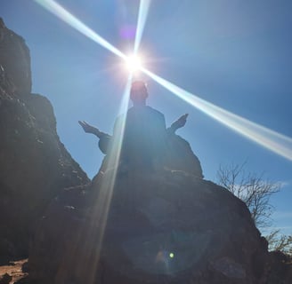 The silhouette of a person on a mountain meditating with the sun in the background.