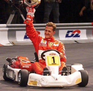 Pilote en tenue Ferrari saluant avec un casque en main dans un kart blanc marqué "KSN"