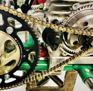 Chaîne dorée et engrenage robuste sur le système de transmission d’un kart, monté sur un axe métallique vert.