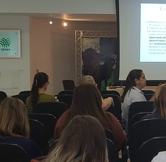 Foto de mulher psicóloga apresentando palestra sobre saúde mental para plateia empresarial.