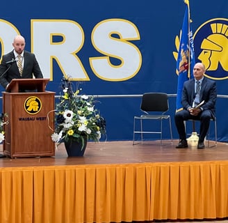 a man standing at a podium with a microphone and a woman sitting at a podium