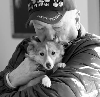 man with navy veteran hat kissing the head of the dog he is holding