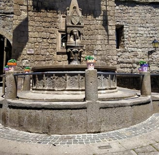 a fountain with a clock on it in front of a stone building