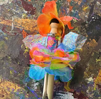 flower fairy clothespin doll laying on a paint-splattered table