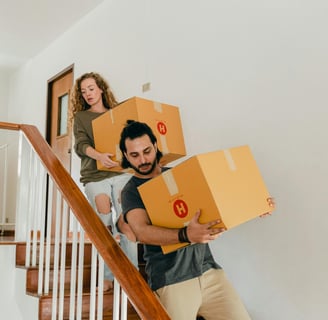 a man and woman moving boxes down stairs