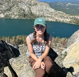 the author sitting on a rock in the mountains. in the background is a lake and a forest of pine.