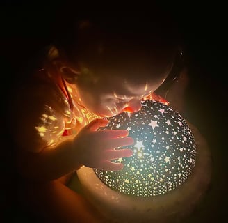 Baby gazing into a blue starry night light, with yellow stars casting on her, as if peering at a new world.