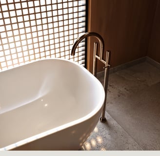 Minimalist white freestanding bathtub, bronze floor-mounted faucet.