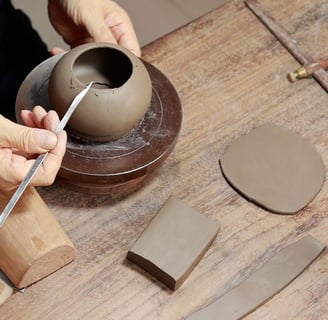 A man holding a long-handled pointed knife, carving the edge of a Yixing teapot