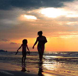 Retrato de una madre y su hija caminando por el agua de la playa en un atardecer