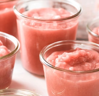 Clear jars containing pink rhubarb applesauce