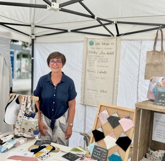 La créatrice derrière son stand sur un marché de créations artisanales