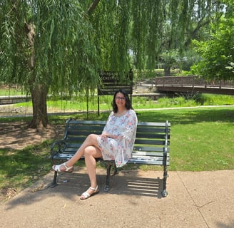 Angela sitting on a bench in the park under a tree.