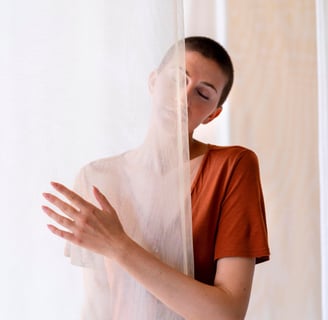 Woman with shaved hair, closed eyes, wearing terracotta clothes, half-body covered by fabric