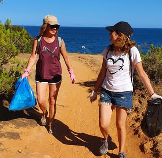 Two female volunteers collecting trash from the sand, cleaning up the beach in Alvor