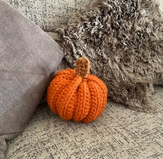 Handmade crochet pumpkin on a sofa with two cushions.