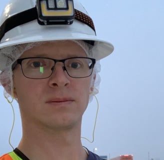 Tomkins dressed in a safety vest and hard hat standing outside on a snowy day. 