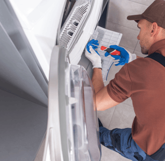 a man in overalls and a hat, working on a refrigerator
