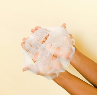 someone holding a beauty face mask with both hands against a yellow wall.