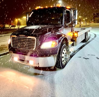 a tow truck with a flat bed in the snow at night with its lights on