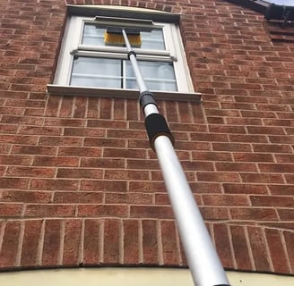 brush on an extension pole cleaning a window on a house in droitwich