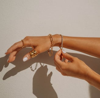 Foto de mão com pulseiras e anéis em dourado.