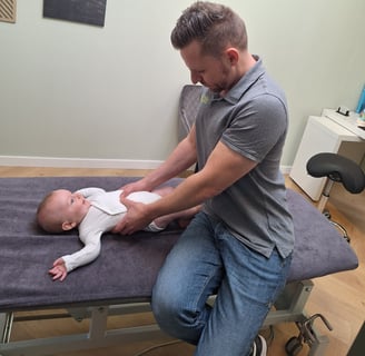 een man geeft een manuele behandeling aan een baby in zijn buik
