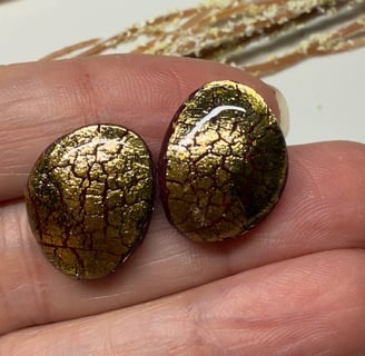 a person holding two gold earrings with gold foil