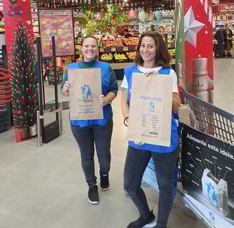 Two female volunteers helping with a food bank campaign in Alvor, holding bags for food donations