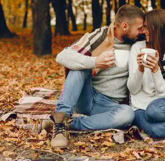 a man and woman sitting on a blanket in the woods