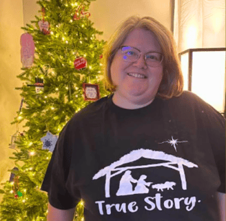 a customer wearing a joyhelpers t-shirt standing in front of a Christmas tree.