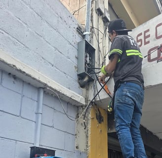 Instalación eléctrica en acometida de edificio por técnico con uniforme.