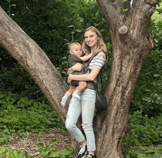 Mother holding baby in a carrier by a tree, bonding in nature.